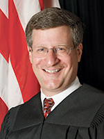 Portrait of white male with glasses and graying hair in judicial robe.